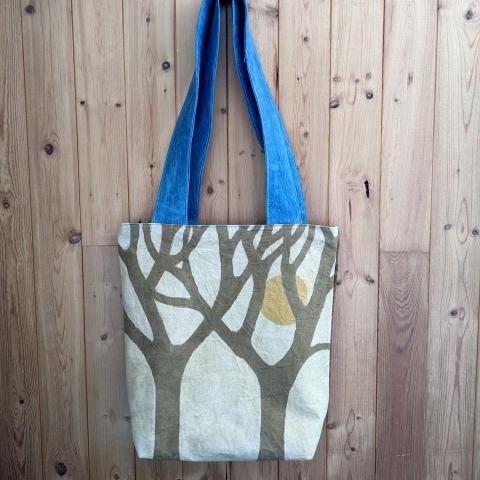 Shoulder bag with stylized trees and a sun hanging on the wall.