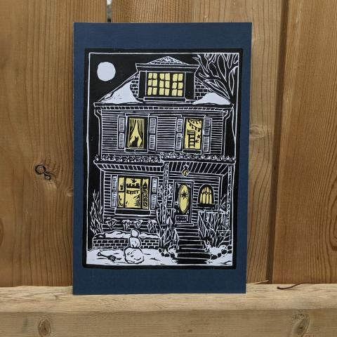 Card Showing the outside of a house with lit windows at nightime around Christmas