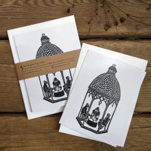 Package of 5 cards showing a linocut of three people gathered around a tealight in a little lantern.